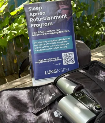 Une machine à apnée du sommeil est posée dehors sur une table de pique-nique entourée de feuillage vert.