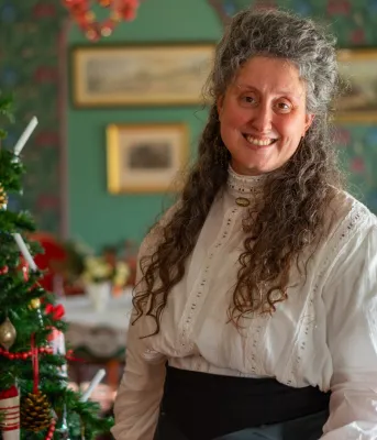 Une femme aux longs cheveux gris sourit devant un sapin de Noël.