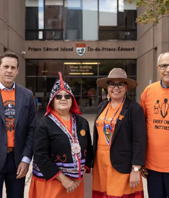 Le Premier ministre et trois autres sont debout ensemble portant des chemises orange.