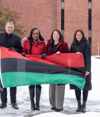 Four people stand behind a red, black and green flag striped.