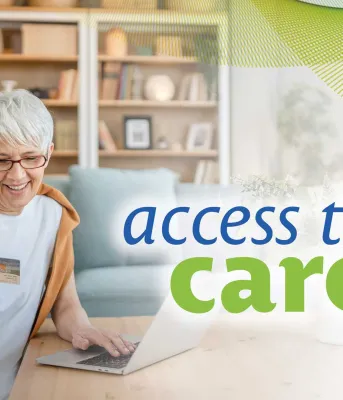 A pharmacist smiles at a customer across a counter in a well-stocked pharmacy with shelves of medications and a sign reading "PRESCRIPTIONS."