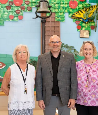 Two women and a man stand in front of a colorful mural.
