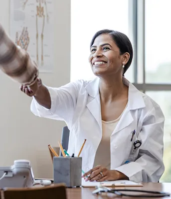 Smiling female doctor sitting at their desk greets patient by shaking their hand
