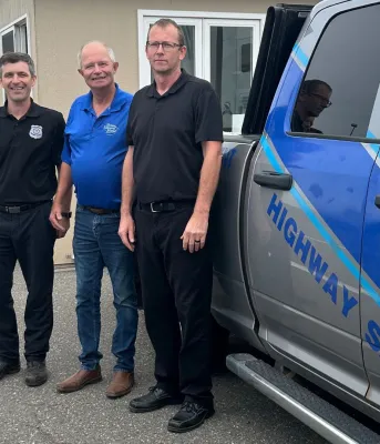 Three men stand in front of a Highway Safety Truck.