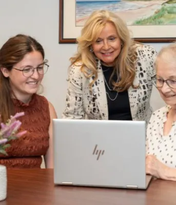Une femme âgée et deux autres femmes se rassemblent autour d'un ordinateur.