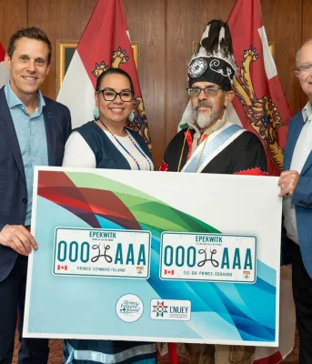 Four people stand behind a sign depicting the new license plate design.