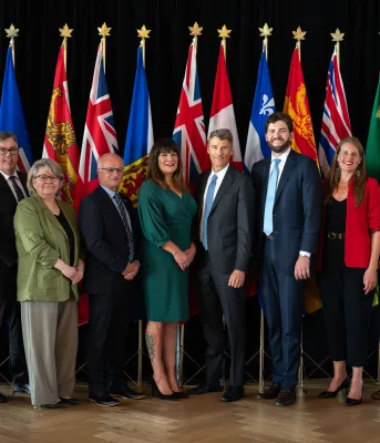 The ministers stand together in front of flags from each province.