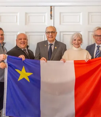 Seven adults hold a large Acadian flag.