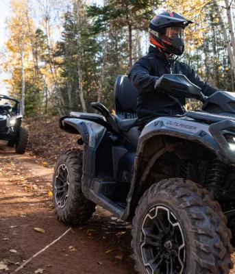 Two ATVs drive down a red dirt road in Autumn.