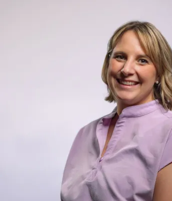 Une femme aux cheveux blonds mi-longs portant une tenue médicale rose.