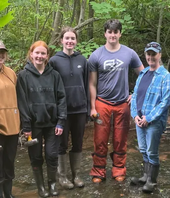 The Minister and watershed staff stand in the river with green foliage behind them.