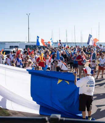 Many people celebrating in front of a large Acadian flag.