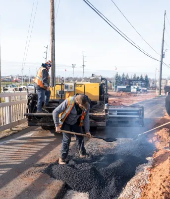 Three construction workers placing asphalt on an active transportation pathway in Prince Edward Island.