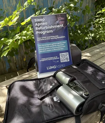 A sleep apnea machine on a picnic table outside, with green foliage in the background.