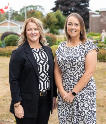 Two women stand next to each other outside.