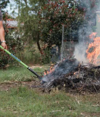 man raking a pile of burning leaves