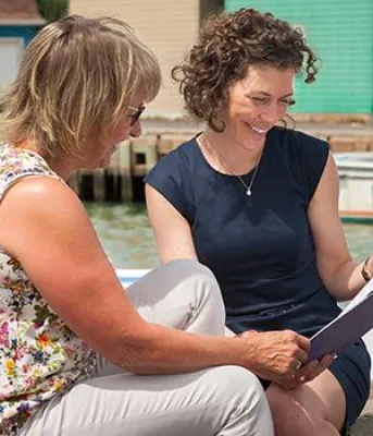 Image of two women sitting on dock at a PEI fishing harbour looking over a brochure