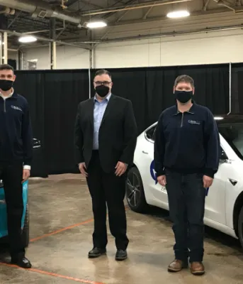 Four Electric Vehicle reps stand in front of two electric vehicles in a convention facility