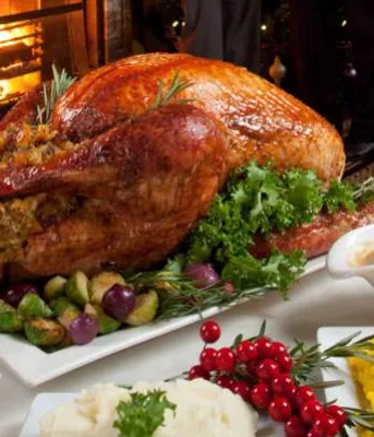 Image of dinner table set with roasted turkey, mashed potatoes, cranberry sauce and pickles