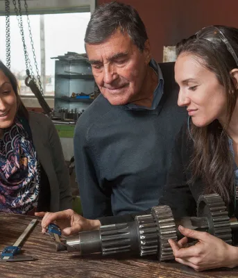 Three people looking at a machine part and measuring its size.