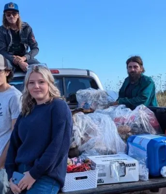 image of a group of people siting on and standing around a truck parked near the shore