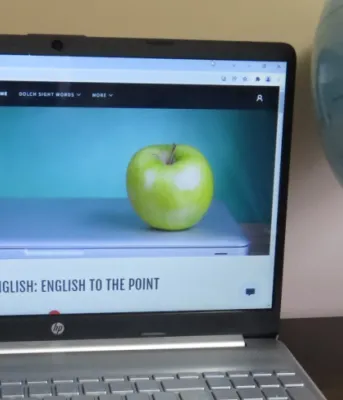 The photo shows a laptop computer  on a table. The computer is open showing the Better English webpage. 