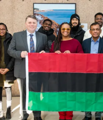 image of people standing shoulder to shoulder with a large flag in front of them