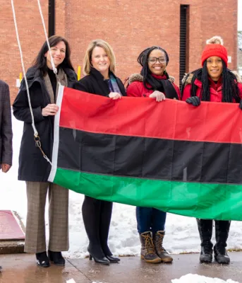 image of a group of people standing shoulder to shoulder holding a flag before it is raised up a flagpole