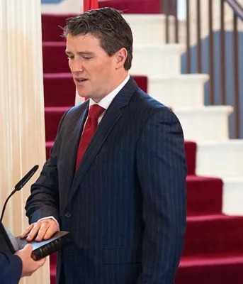 Photo shows Jordan Brown taking the oath from Paul Ledwell with Premier MacLauchlan looking on.