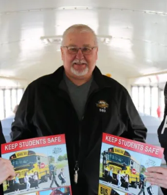 Three people stand inside a school bus holding school bus safety posters