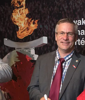 Brian McFeely holds a 1991 Canada Games jacket, Health and Wellness Minister Robert Henderson and Wayne Carew hold a 2009 Canada Games jacket at announcement