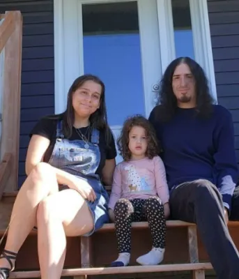 image of two adults and a child sitting on the stairs of a porch in front of a house