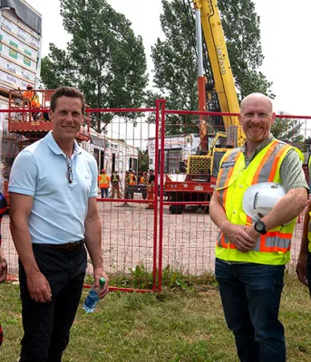 image of six people standing in front of a construction area fence with workers in the background