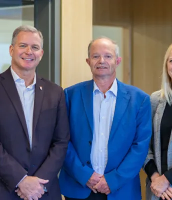 image of three people standing shoulder to shoulder in a room with a wall behind them