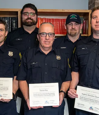 image of a group of people in a room, standing shoulder to shoulder with some holding certificates and book cases in the background