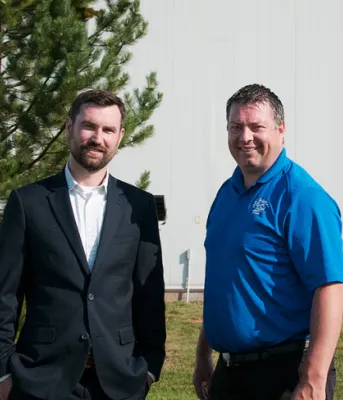Two people standing shoulder to shoulder in front of a building