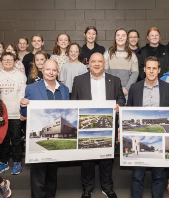 image of a group of students with three adults in front of them holding design renditions of a school
