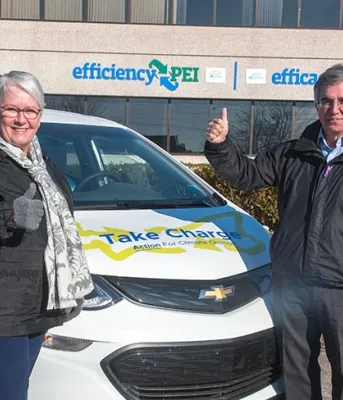 Four people stand beside an electric car in front of the efficiencyPEI building