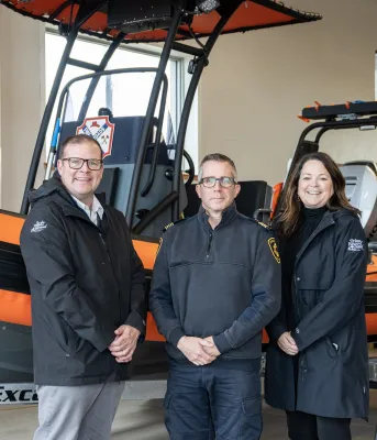 image de trois personnes devant un petit bateau de sauvetage dans un garage