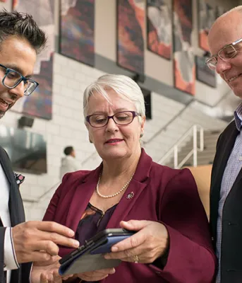 Photo shows three people looking at an app on a tablet