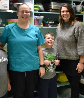 Photo shows two grade three students standing with two adults in a kitchen environment