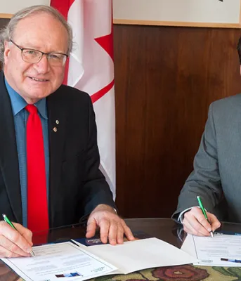 Premier MacLauchlan and Jese Francis sitting at a desk signing documents.