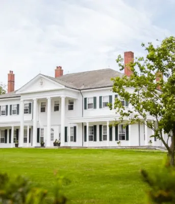 image d'une grande demeure seigneuriale avec une grande pelouse et divers arbres qui l'entourent.