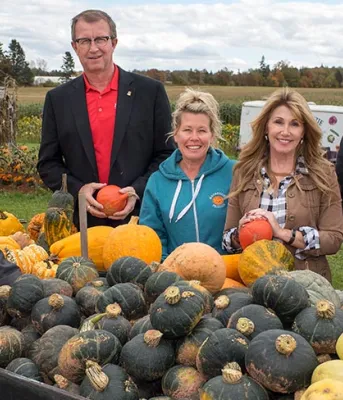 Photo shows a group of six people standing with a cart of pumpkins and gourds.