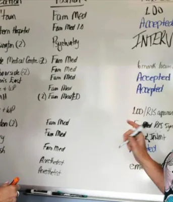 Photo shows two women talking in front of a whiteboard