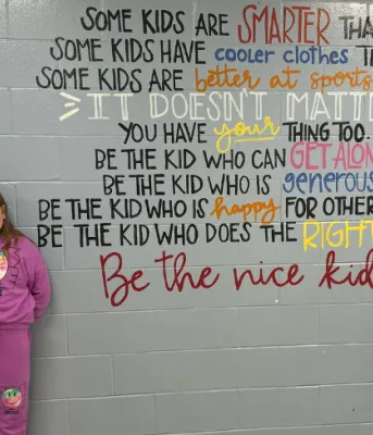image of a teacher and elementary students standing near a wall with some inspirational writing on it.