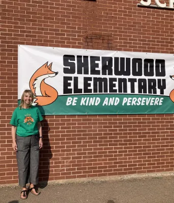image of a person standing in front of a brick wall with a sign behind her
