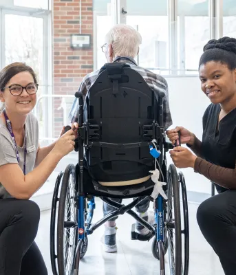 image of two people beside a person in a wheel chair inside a building foyer
