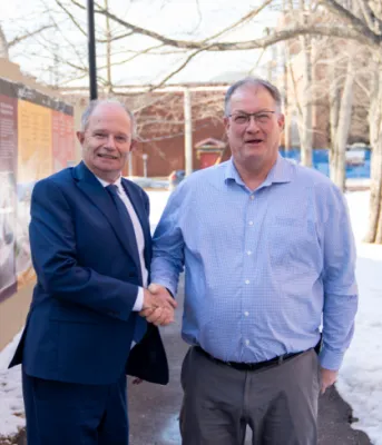 image de deux personnes debout à l'extérieur près d'un mur en bois se serrant la main avec quelques arbres en arrière-plan