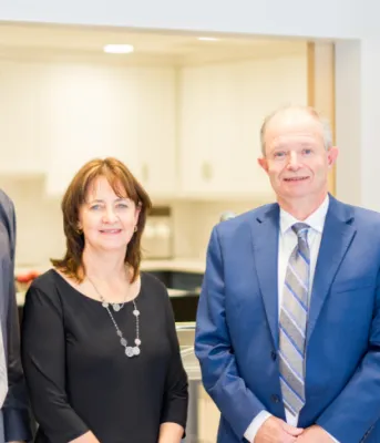 image of four people standing shoulder to shoulder in a room with a PEI flag behind them